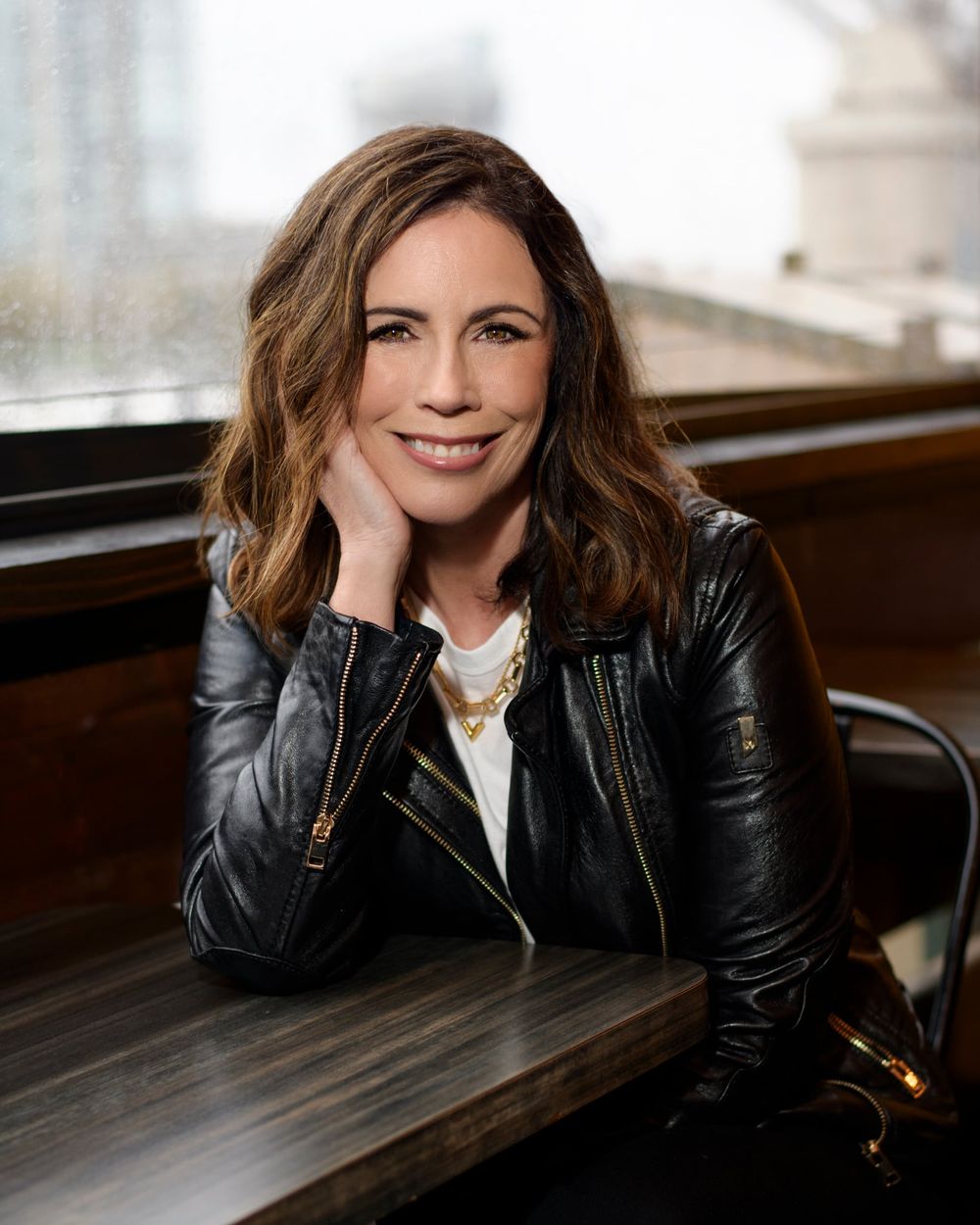 Valerie Jones in a black leather jacket, resting her chin on her hand and smiling at the camera
